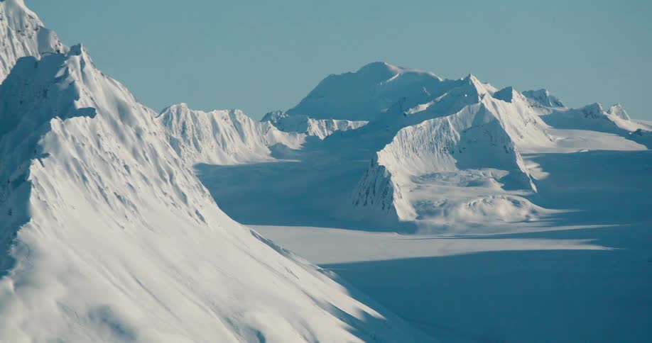 A sweeping alpine panorama shows jagged snowdraped peaks and a broad glacierfilled valley beneath a clear cold sky
