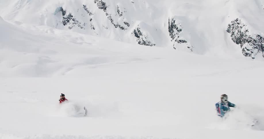 Three people ride snowmobiles across a snowcovered slope