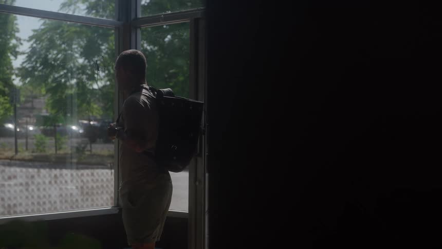 Man with a backpack looks at the street through a sunlit glass door