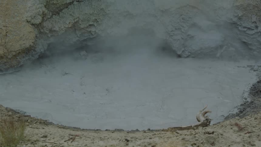 Geothermal mud pool releasing steam on cracked ground