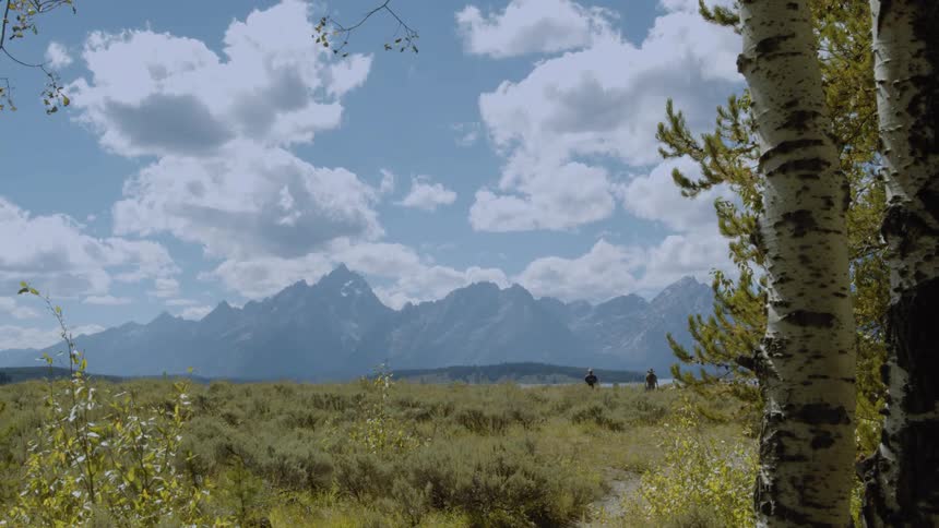 Two people walk in the wilderness near a mountain and flatland