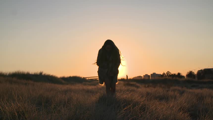 Woman walking through a grass field at sunset
