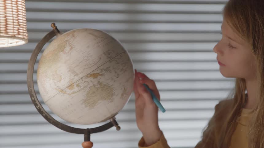 A young girl studies the surface of a globe as she slowly rotates it