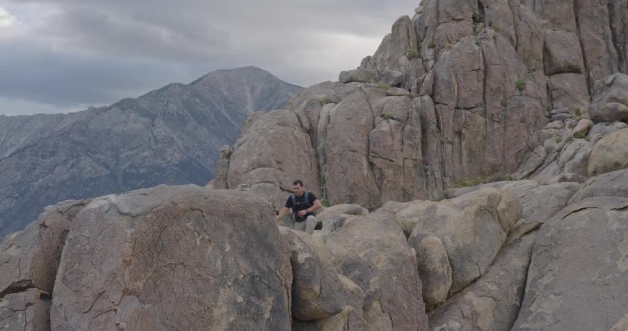 A hiker climbs through rocky mountain terrain under cloudy skies