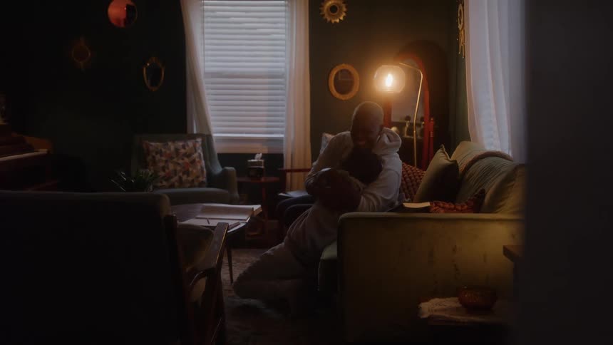 Two people embracing in a room lit by soft light at dusk