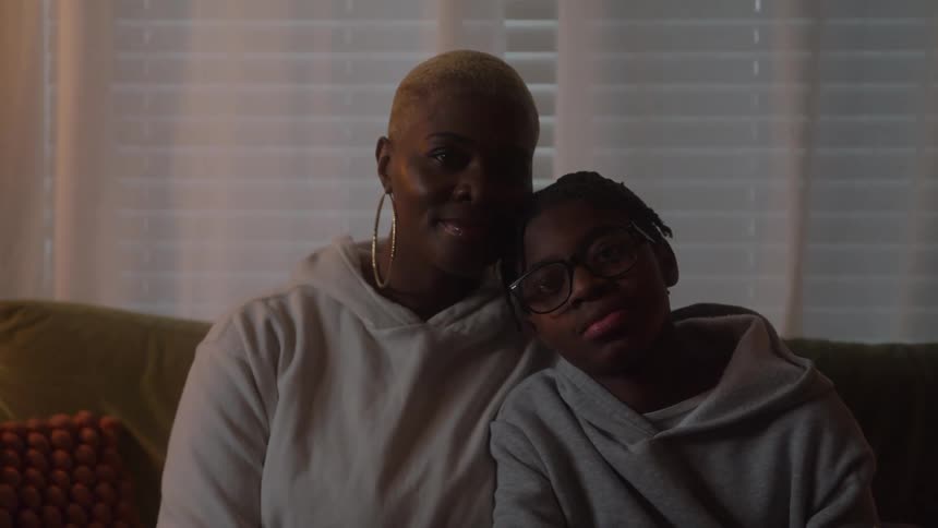 Mother and son sit on a couch smiling warmly in a cozy living room