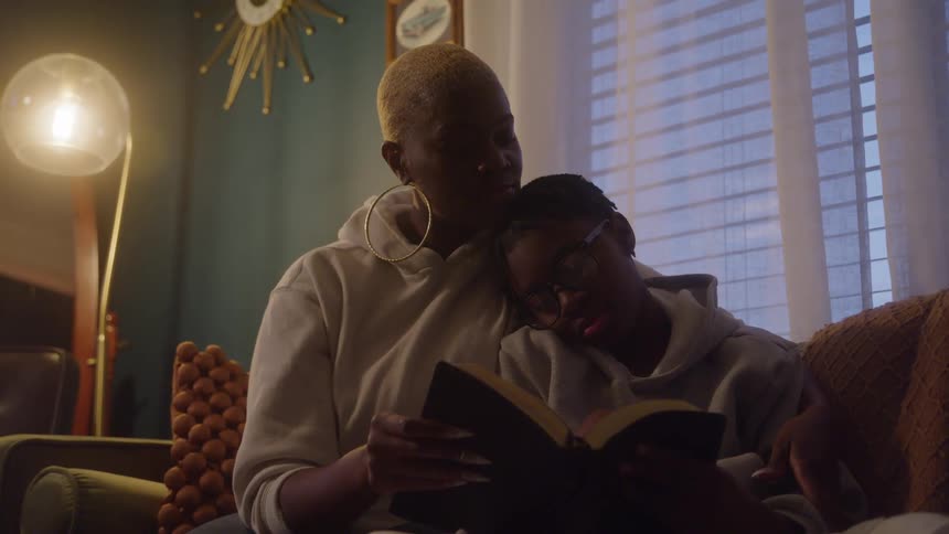 Mother and son read together on the couch sharing a peaceful moment at dusk