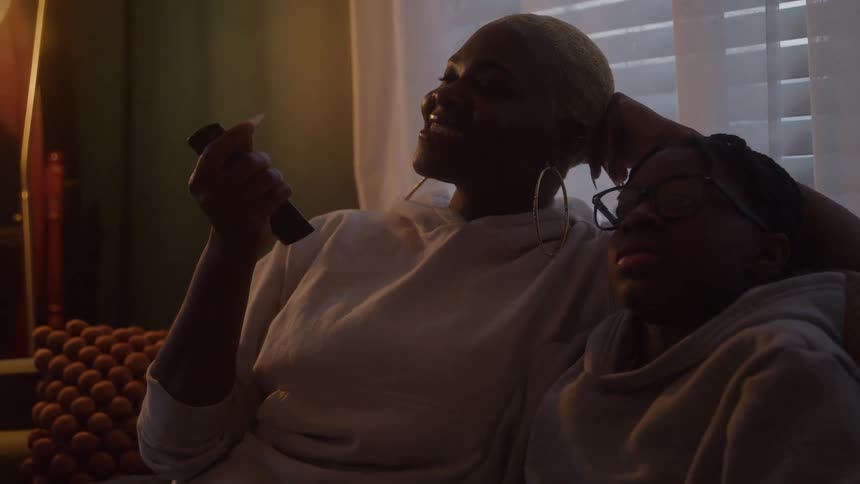 The mother smiles while changing channels with the remote