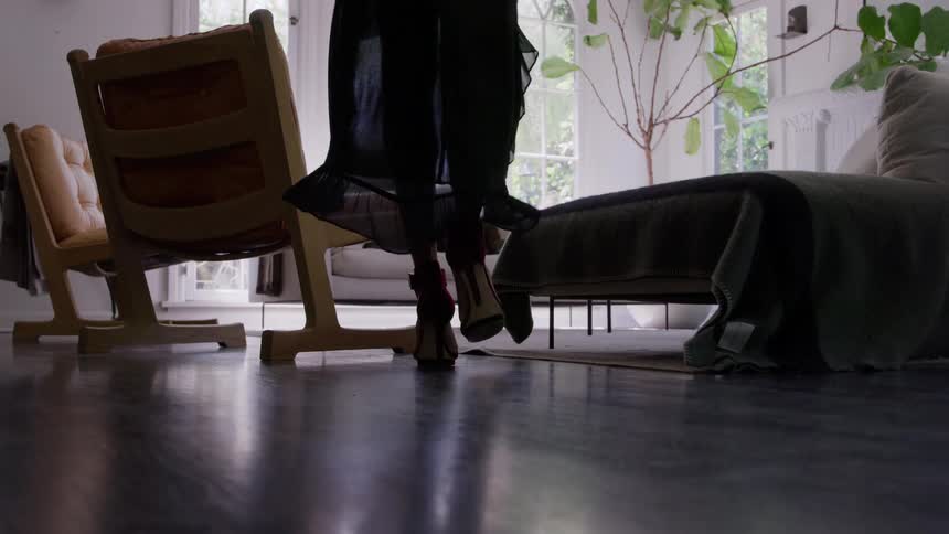 Woman wearing high heels and a filmy outfit walks through a room at home during the daytime