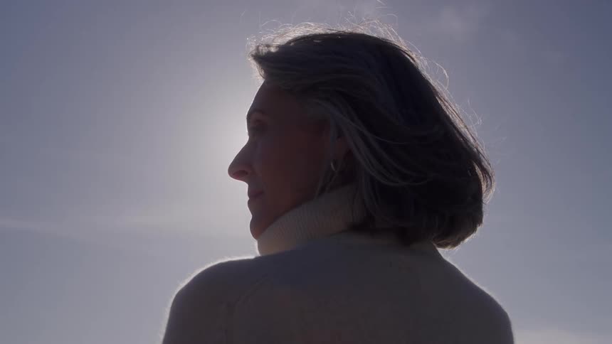 Woman standing outside on a sunny day smiles as the wind blows her hair