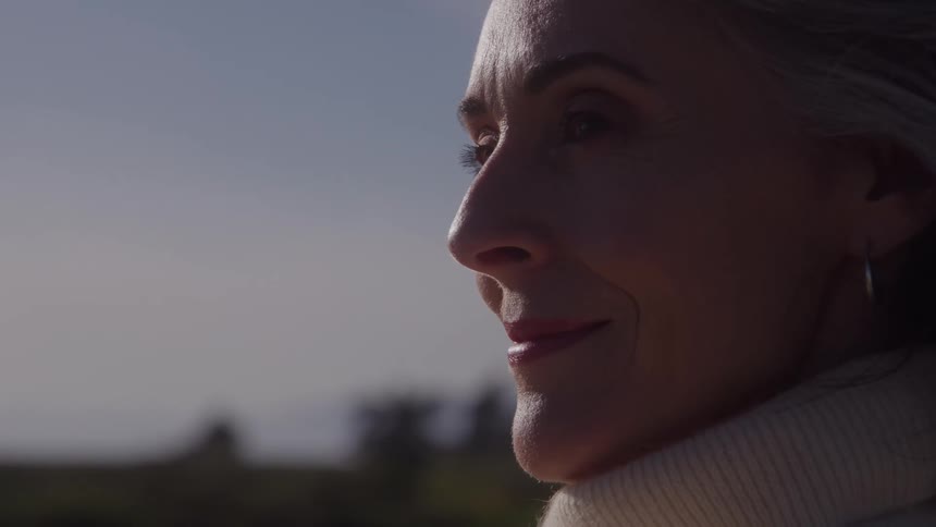 Grayhaired woman smiles softly while gazing at the horizon outdoors
