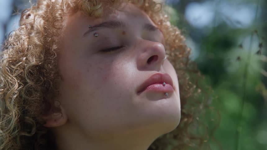 Woman with closed eyes feels the warmth of the sun among the greenery