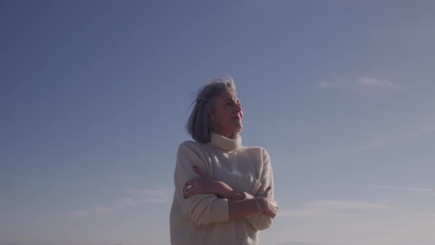 Woman in a light sweater crosses her arms while gazing at the open sky