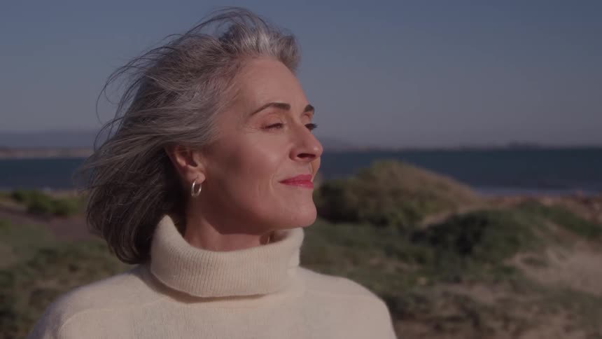 Woman smiles on a beach with the ocean behind under bright sunlight