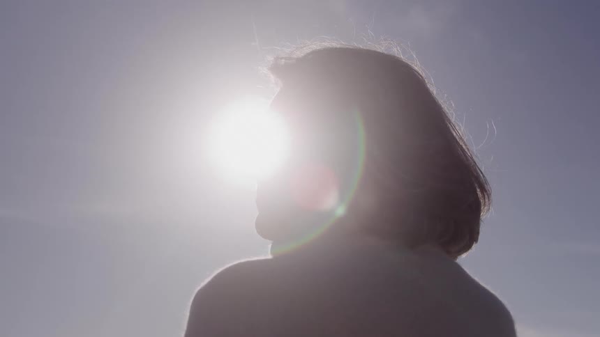 Grayhaired woman is illuminated by the sun as she looks toward the horizon