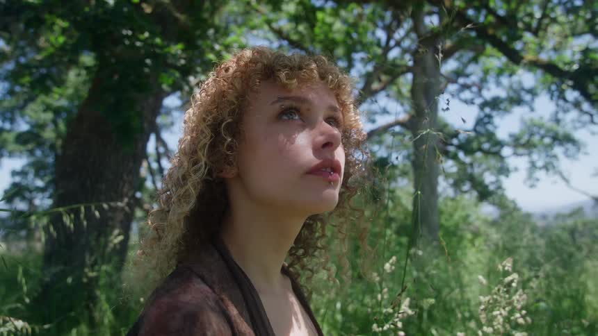 The woman is looking up in the woods