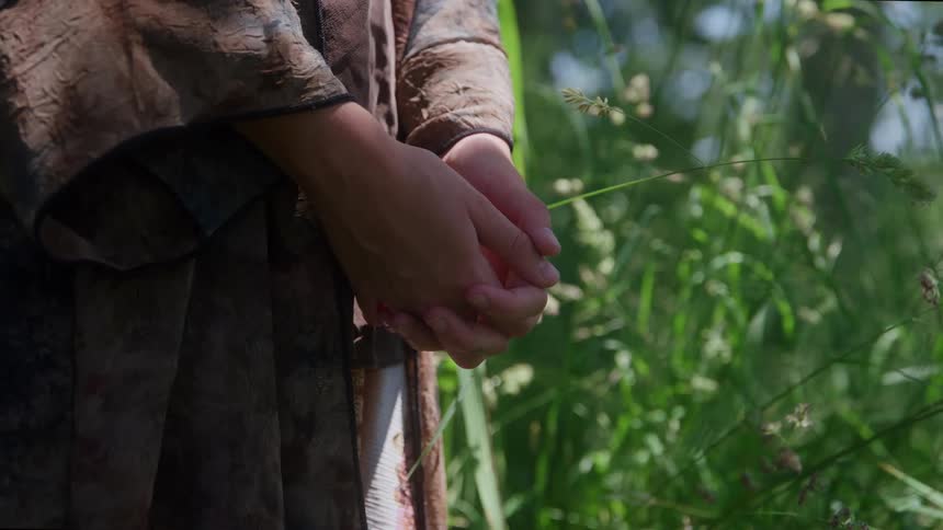 Person keeps their hands clasped among sunlit vegetation
