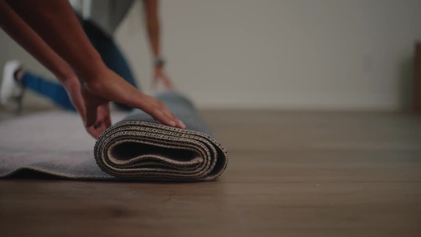 A womans hands are unrolling a yoga mat on a wooden floor