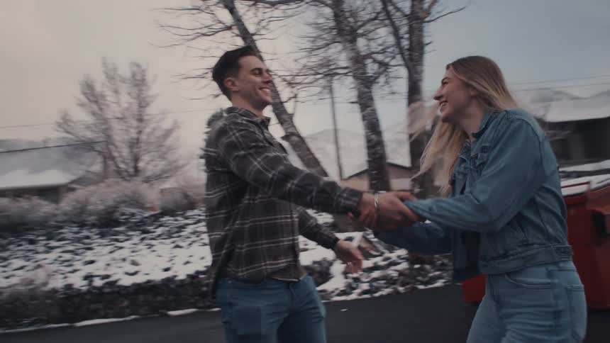 A happy couple hold hands and spin around on a suburban street