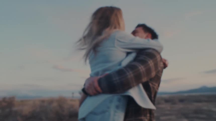 A man lifts and embraces a woman in his arms on grass covered land