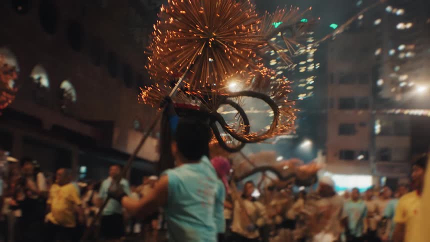 Men parade with a fire dragon surrounded by glowing sparks