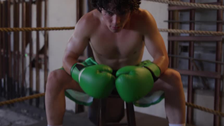 Boxer with green gloves looks with a determined expression inside the ring