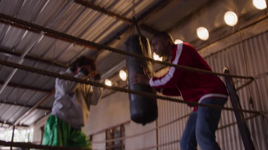 Coach holds the punching bag while the boxer practices fast punches in the ring