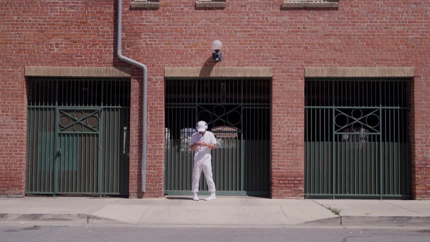 Man dressed in white dances alone in front of a brick building under the sun
