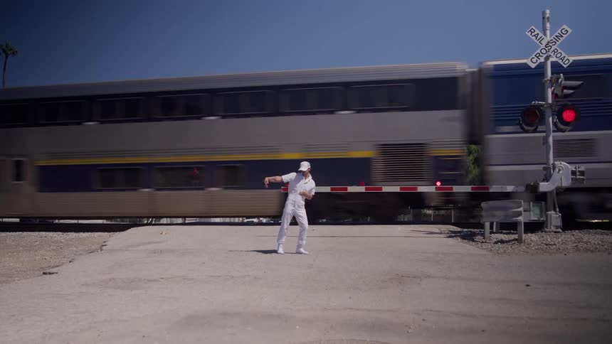 A young male dancer dancing outdoors in front of a railway in a metropolitan city during daytime
