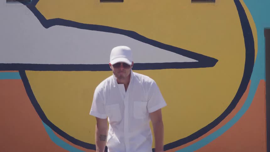 A young man dancing outdoors in front of a graffiti wall during daytime