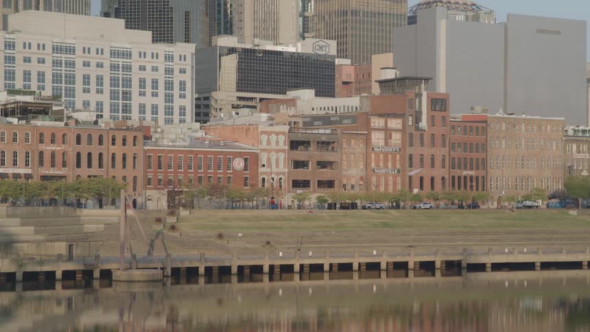 Urban view of historic and modern buildings by a river with reflections on the water and a grassy area in the foreground