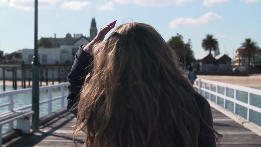 Woman walking along a pier puts her hand through her hair