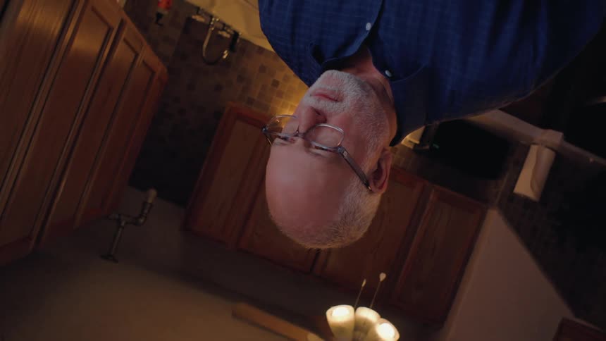 An older man stands holding a glass of orange juice in a kitchen