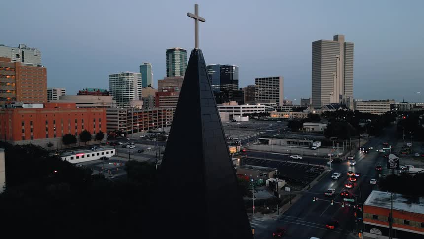 Vehicles move along the downtown streets near a church after dusk