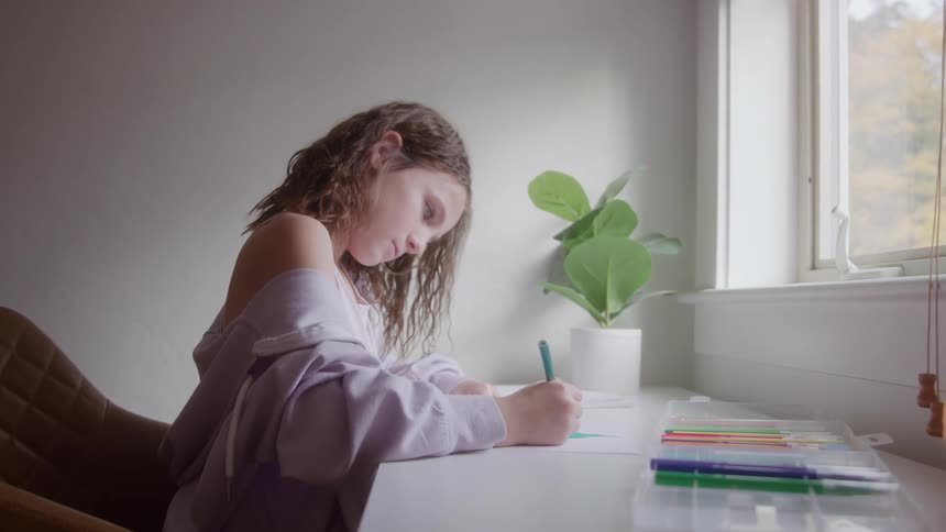 A girl working on a school project at a sunlit desk by the window