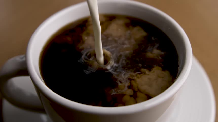 Milk being poured into a cup of black coffee creating swirls on the surface