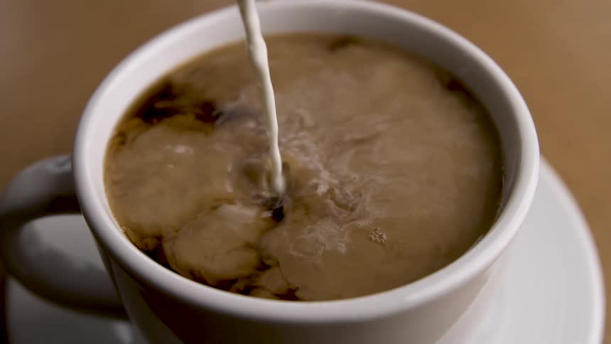 Milk is poured into a cup of coffee