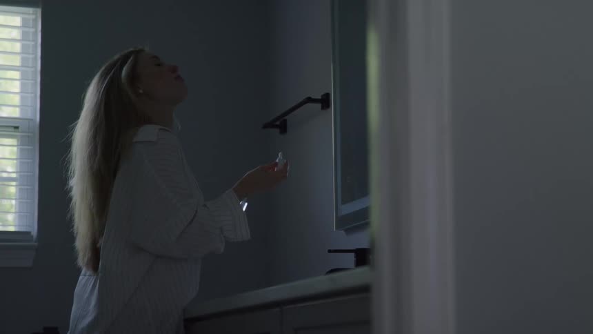 Woman applying lip gloss in front of a bathroom mirror