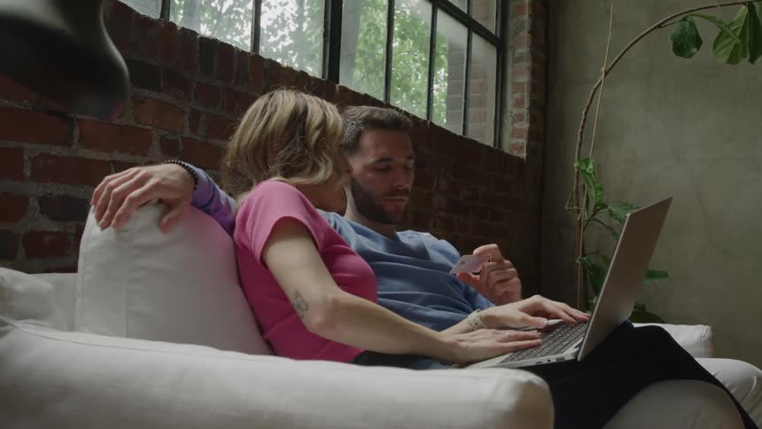 Couple sitting on the couch using a laptop while the man holds a card