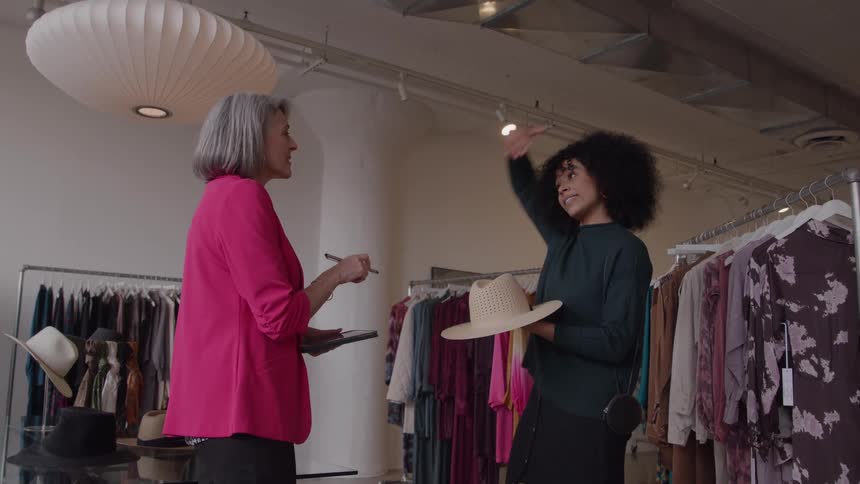 A store assistant helps a client try on a hat in a modern boutique