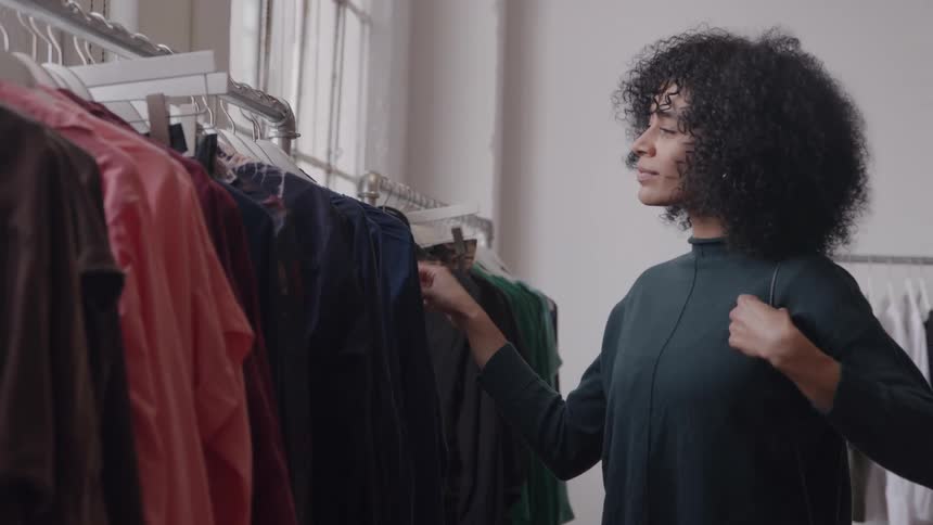 A black female happily shops through a clothing rack in a boutique