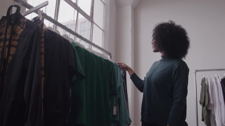 A woman is browsing a rack of clothes in a brightly lit boutique