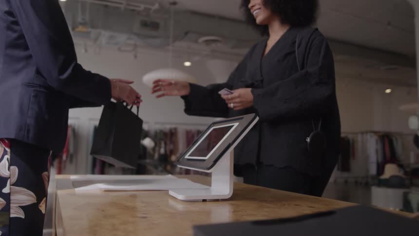 A sales woman cashes out a customer in a clothing store and hands her a bag