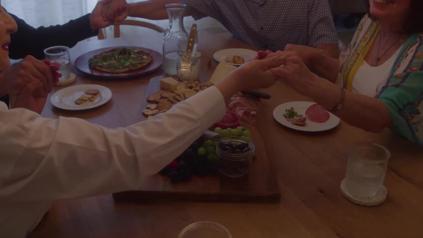 A group of friends or family holds hands to say grace around a beautifully set dinner table before their meal
