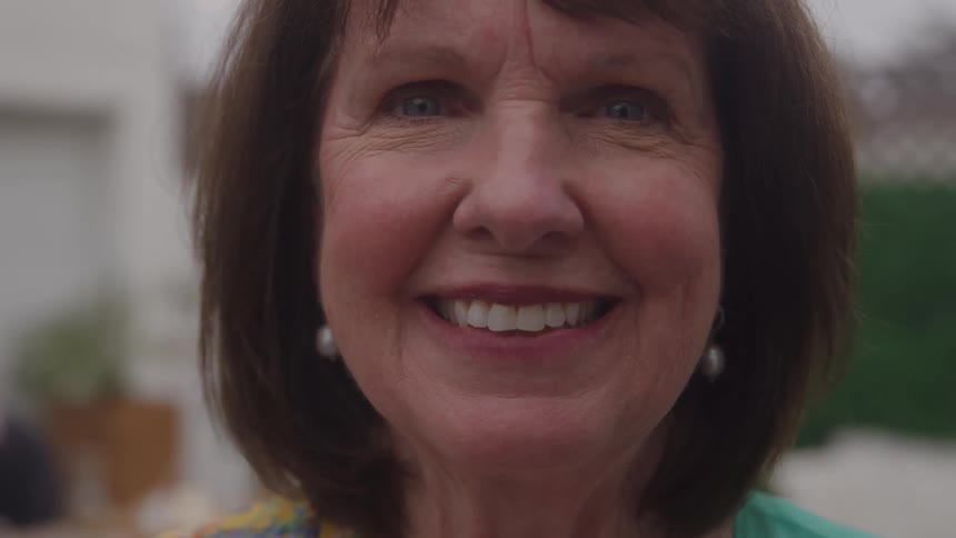 A middleaged woman smiles broadly outdoors at midday