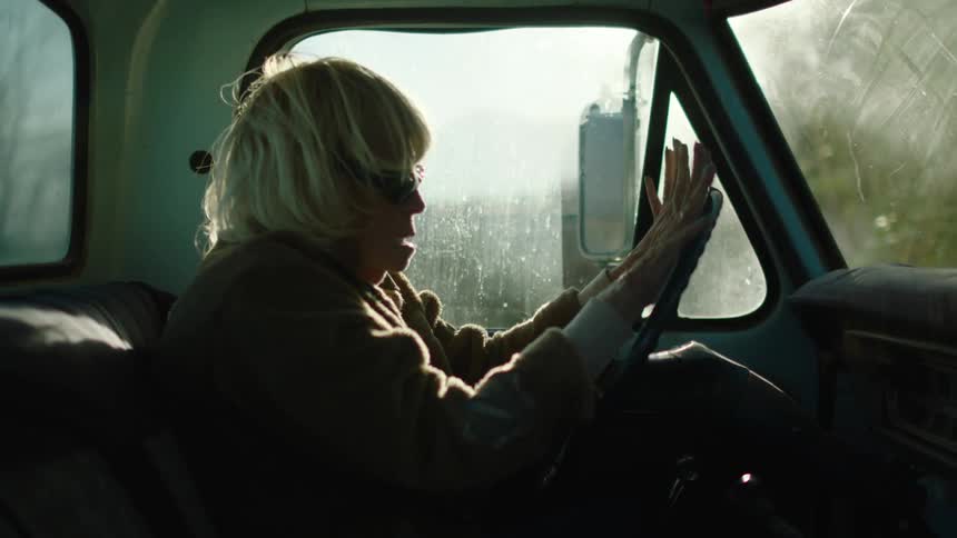 An old woman with dark glasses on is driving a truck