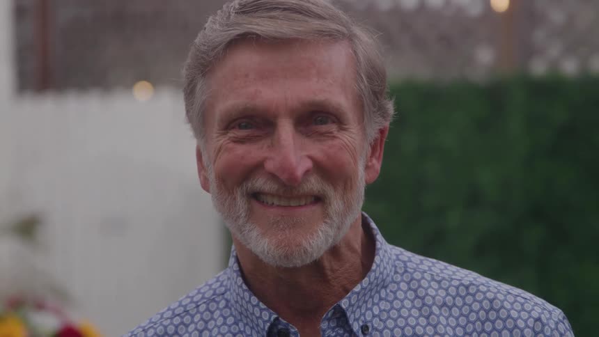 Graybearded man smiles wearing a patterned blue shirt