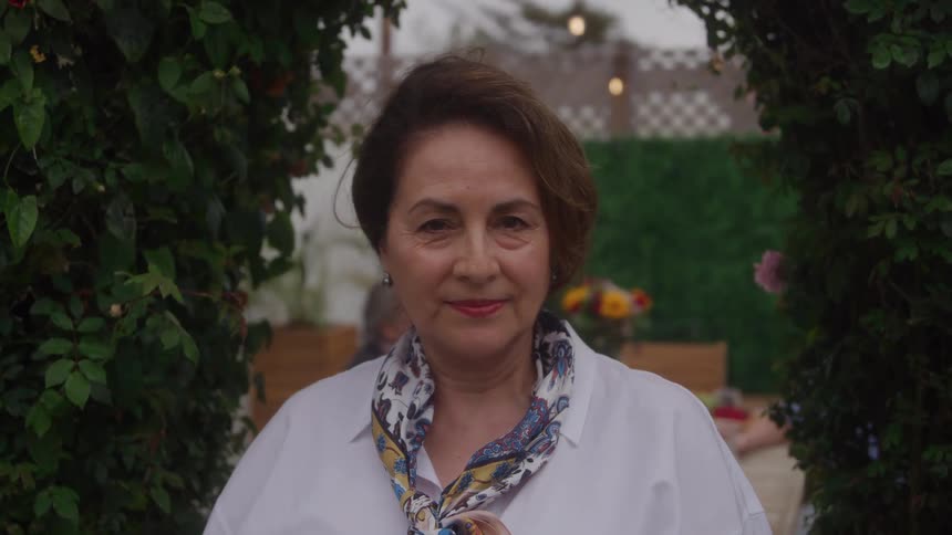Older woman wearing a white shirt and patterned scarf posing outdoors
