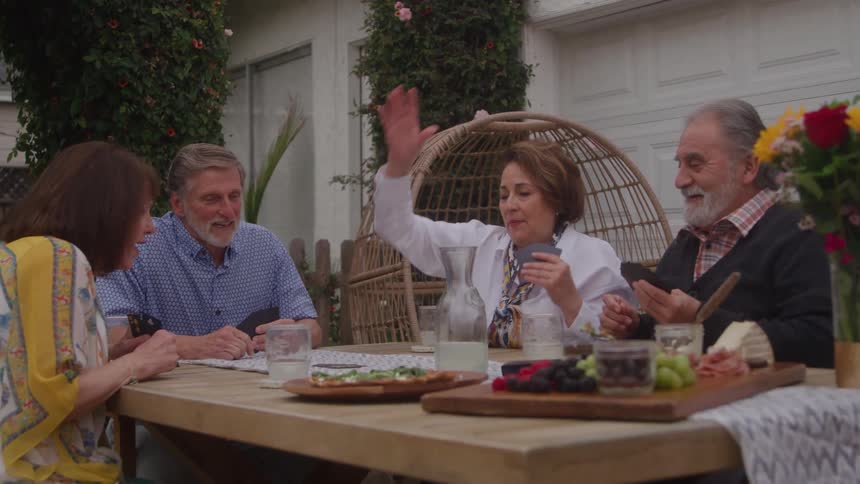 Group of older people sitting at a table playing cards outdoors