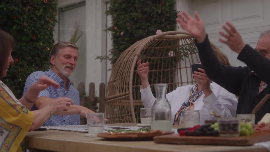 Four older people sitting outdoors laugh while playing cards